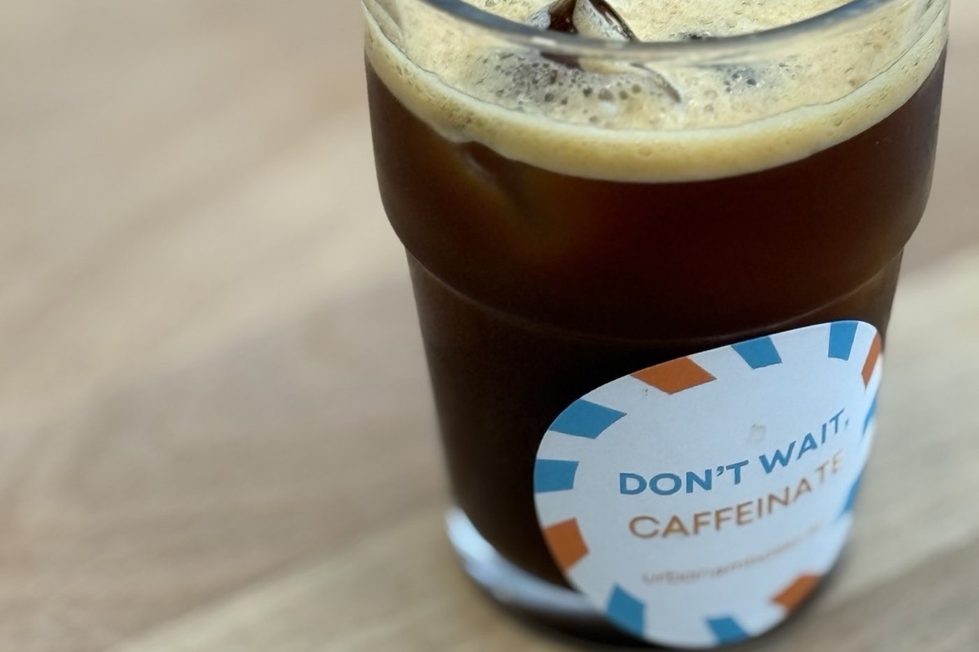 Iced coffee in a glass tumbler with a sticker reading DON'T WAIT, CAFFEINATE