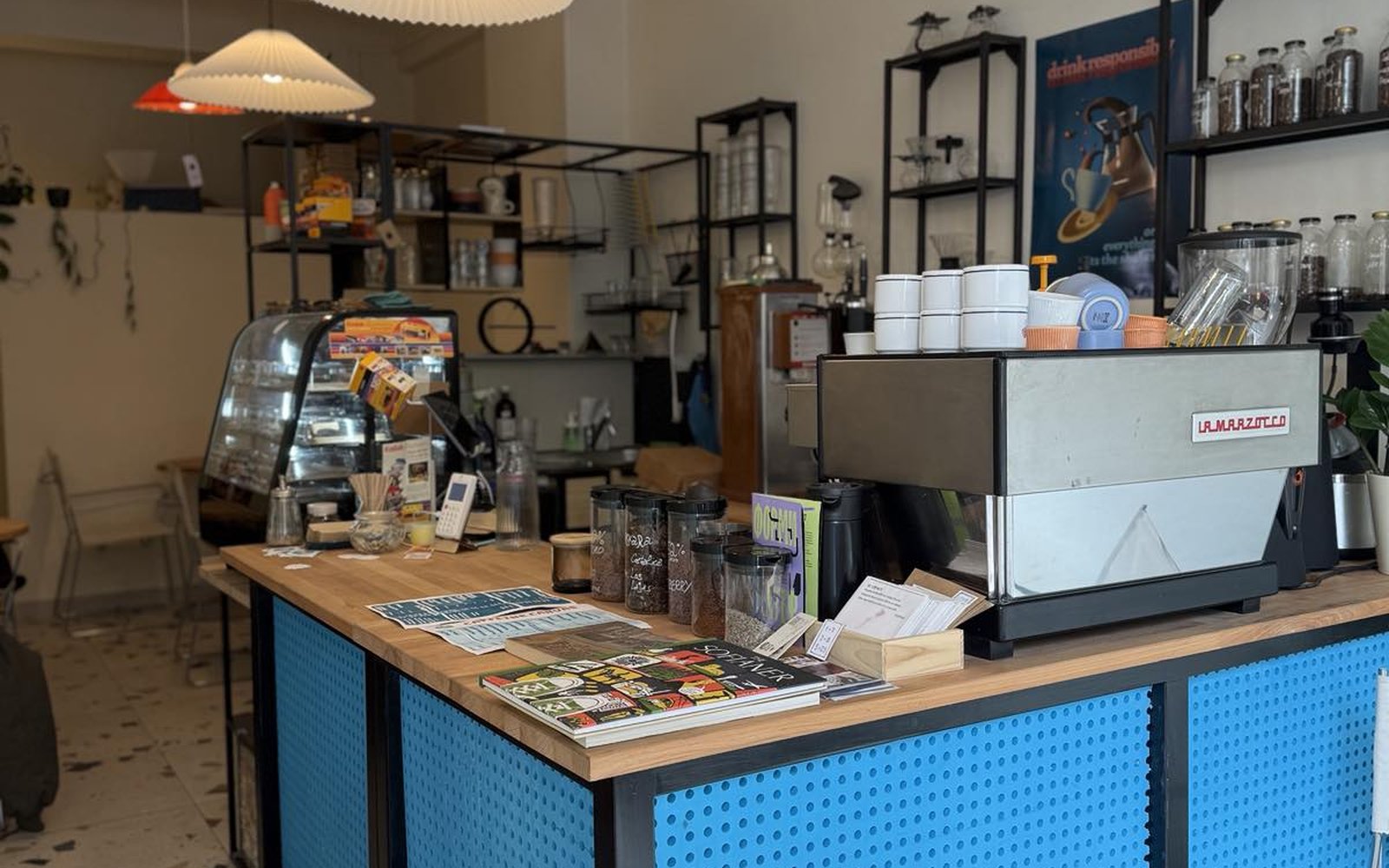 The Urban Embassy counter - blue perforated front, wooden top, a La Marzocco espresso machine and shelves of filter brewing gear